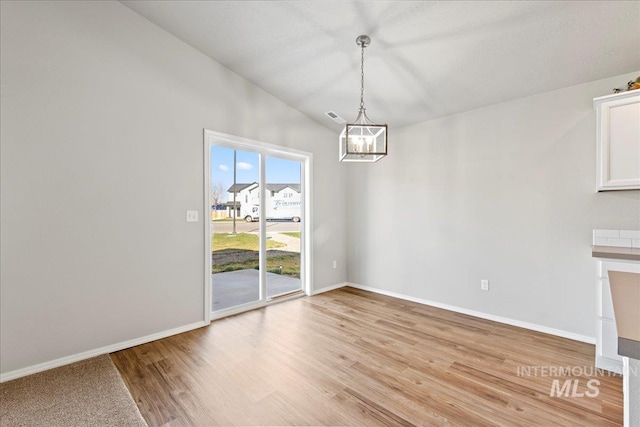 unfurnished dining area featuring lofted ceiling, light wood-type flooring, and an inviting chandelier