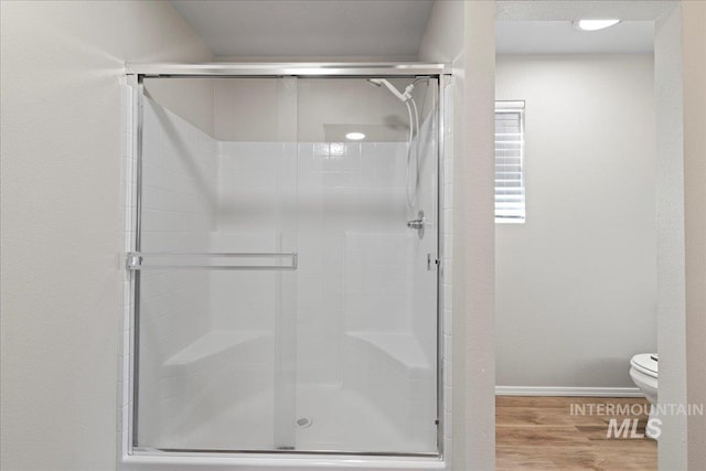 bathroom with a shower with door, hardwood / wood-style floors, and toilet