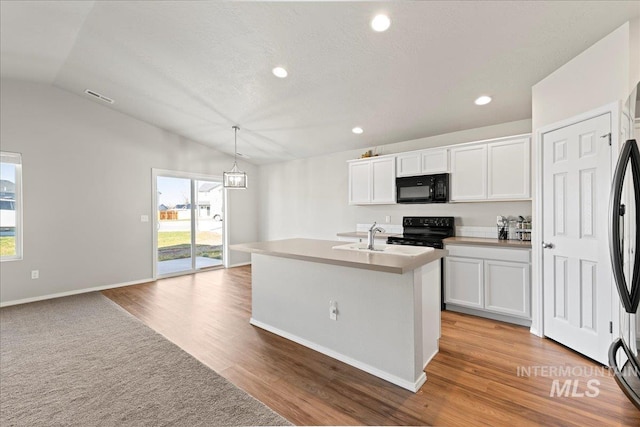 kitchen featuring white cabinets, pendant lighting, a center island with sink, and black appliances