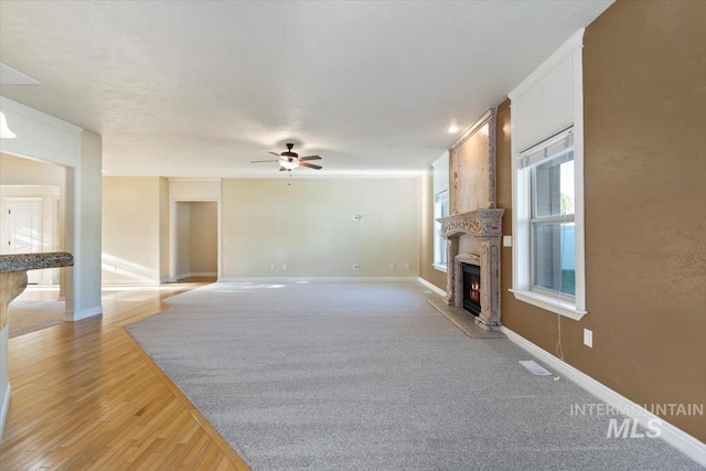 unfurnished living room with a large fireplace, a ceiling fan, light wood-type flooring, and baseboards