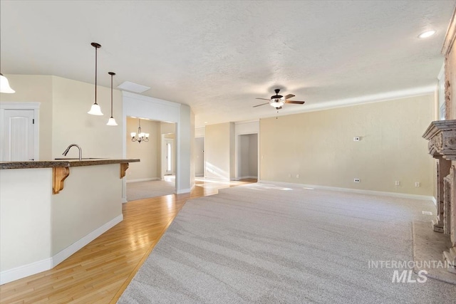 unfurnished living room with a ceiling fan, a chandelier, a fireplace with raised hearth, baseboards, and a textured ceiling