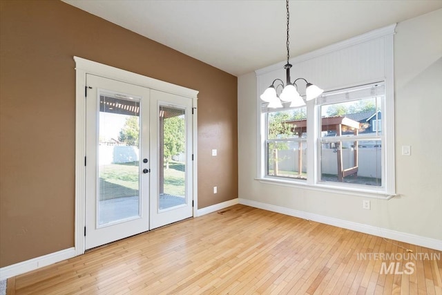 unfurnished dining area featuring french doors, a chandelier, light wood-type flooring, and plenty of natural light