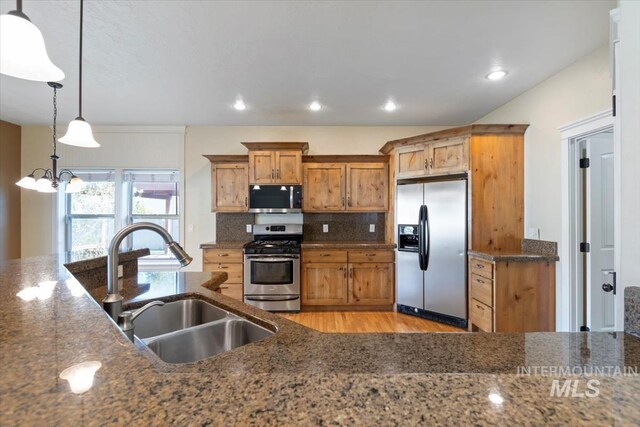 kitchen with appliances with stainless steel finishes, a sink, a chandelier, light wood-style floors, and brown cabinets