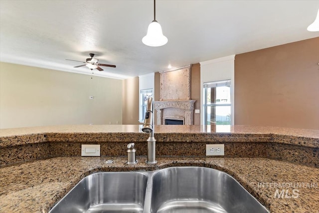 kitchen with a sink, stone counters, a fireplace, ceiling fan, and open floor plan