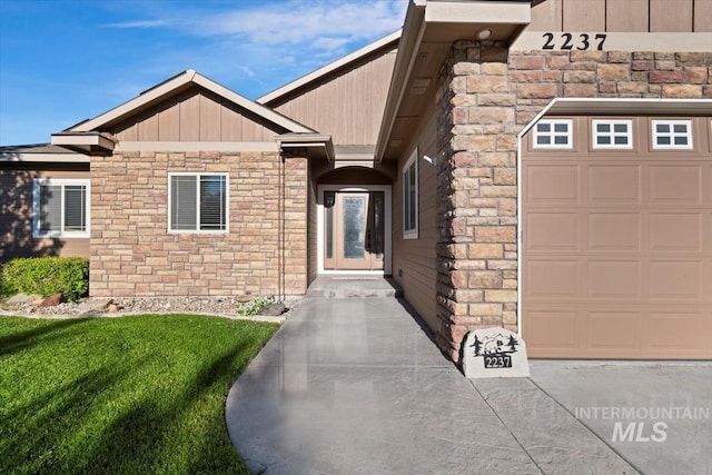 entrance to property featuring a garage, stone siding, a yard, and board and batten siding