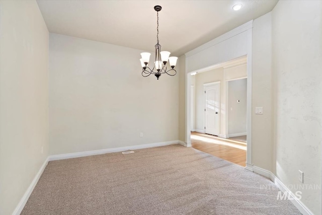 unfurnished room featuring light colored carpet, a chandelier, and baseboards