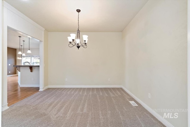 carpeted empty room featuring a chandelier and baseboards