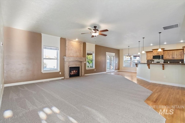 unfurnished living room with a ceiling fan, a large fireplace, baseboards, and light wood-type flooring