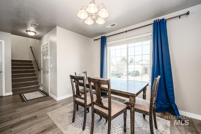 dining space with a notable chandelier, visible vents, wood finished floors, baseboards, and stairs