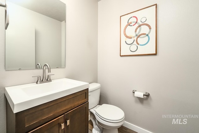 bathroom with wood finished floors, vanity, toilet, and baseboards