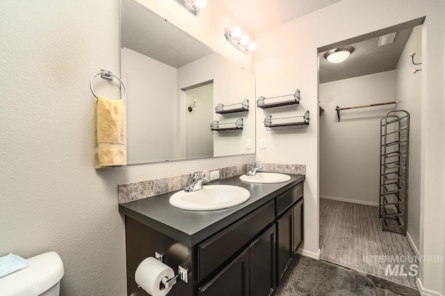 bathroom with baseboards, a sink, toilet, and double vanity