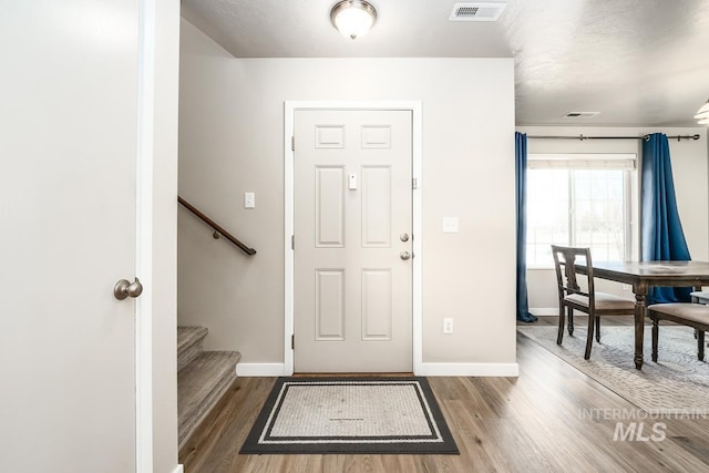 foyer with baseboards, stairs, visible vents, and wood finished floors