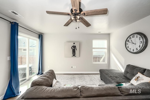 living area featuring a ceiling fan, visible vents, baseboards, and wood finished floors