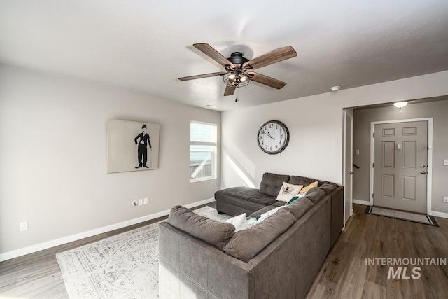 living room with ceiling fan, baseboards, and wood finished floors