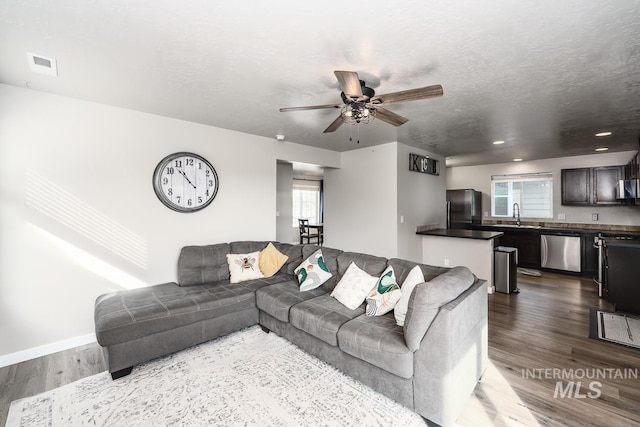 living area with ceiling fan, a textured ceiling, wood finished floors, and visible vents