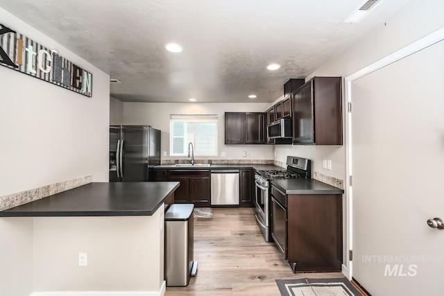 kitchen with a sink, light wood-style floors, dark brown cabinets, appliances with stainless steel finishes, and dark countertops