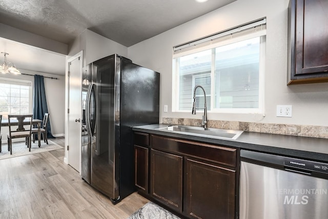 kitchen with dark brown cabinetry, a sink, light wood-style floors, appliances with stainless steel finishes, and dark countertops