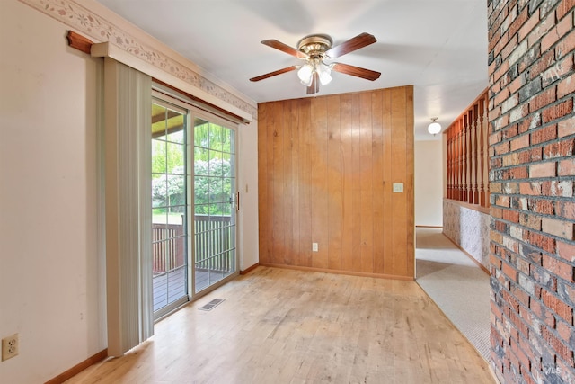 unfurnished room featuring a ceiling fan, baseboards, wood walls, and wood finished floors