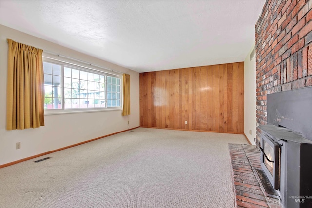 unfurnished living room featuring carpet floors, a wood stove, visible vents, wood walls, and baseboards