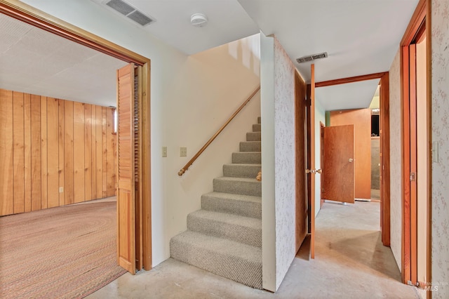 stairs featuring concrete flooring, wood walls, and visible vents