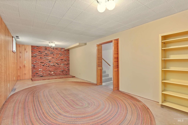 finished basement featuring stairway, wooden walls, and visible vents