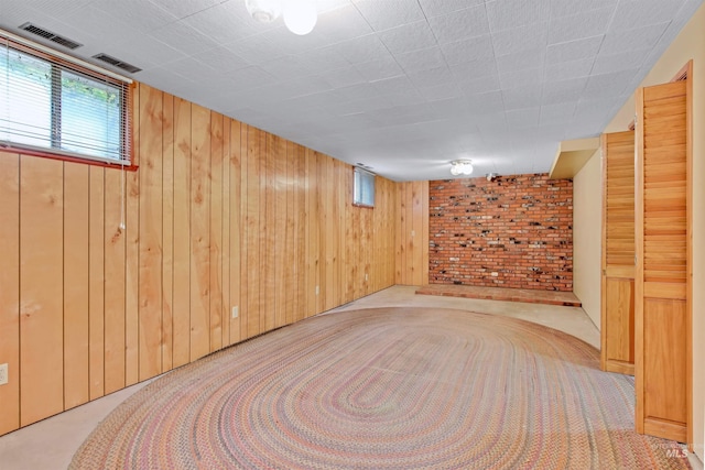 basement with wooden walls, brick wall, visible vents, and carpet floors