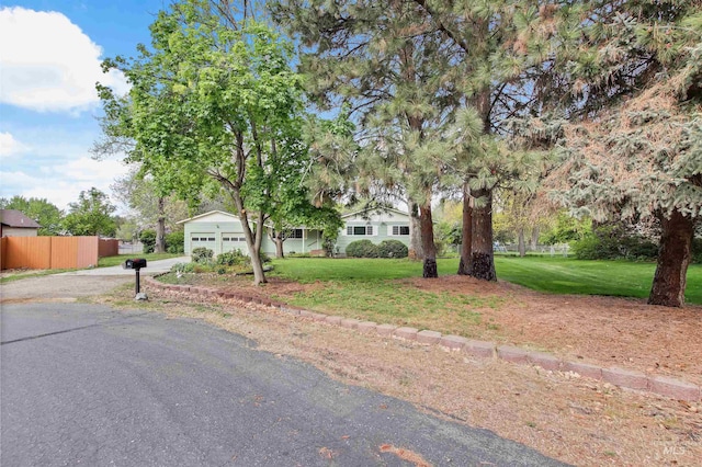 view of property hidden behind natural elements with a garage, fence, driveway, and a front lawn