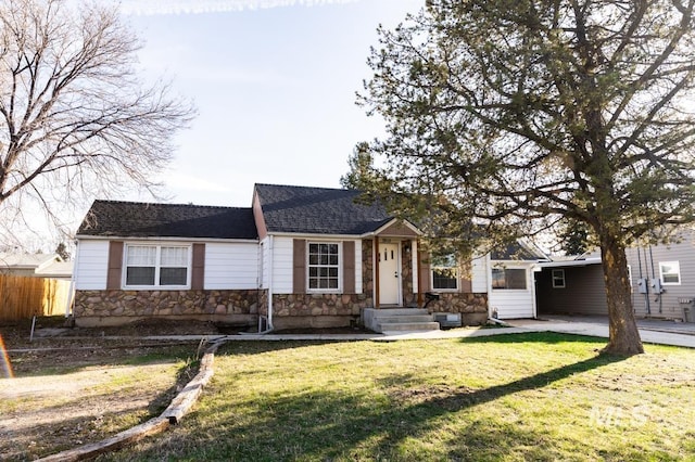 view of front facade with stone siding, a shingled roof, a front lawn, and fence