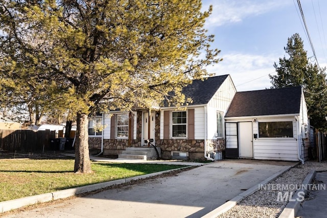 view of front of property with stone siding, fence, a front lawn, and a shingled roof