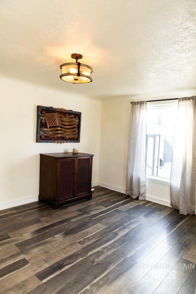 empty room featuring dark wood-style floors, a textured ceiling, and baseboards