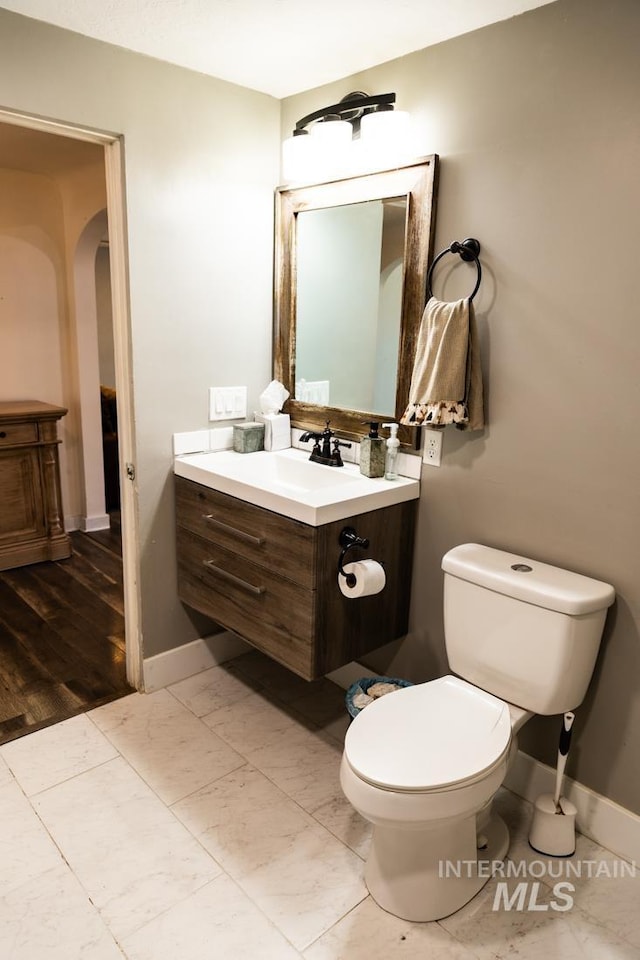 half bathroom with baseboards, marble finish floor, vanity, and toilet