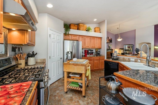 kitchen with appliances with stainless steel finishes, decorative light fixtures, sink, and wall chimney range hood