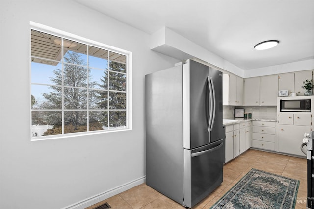 kitchen with built in microwave, a healthy amount of sunlight, light tile patterned floors, and stainless steel refrigerator