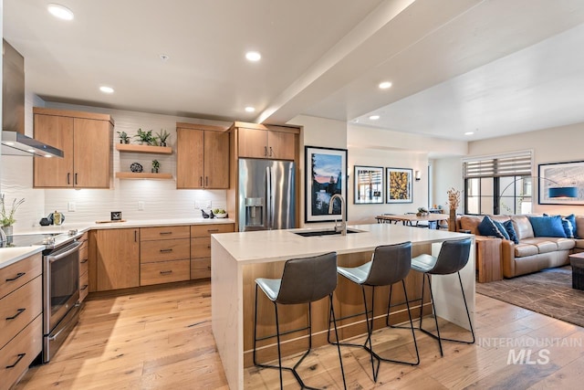 kitchen featuring sink, wall chimney range hood, a kitchen breakfast bar, appliances with stainless steel finishes, and light wood-type flooring