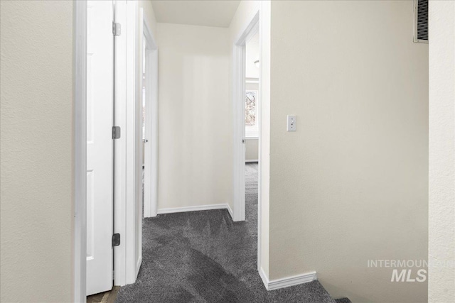 corridor featuring visible vents, baseboards, and dark carpet