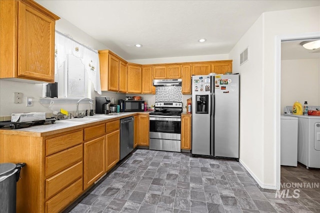 kitchen featuring under cabinet range hood, a sink, appliances with stainless steel finishes, light countertops, and washing machine and clothes dryer