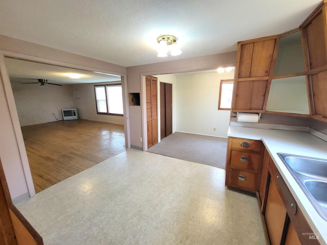 kitchen with a textured ceiling, heating unit, ceiling fan, sink, and light hardwood / wood-style flooring