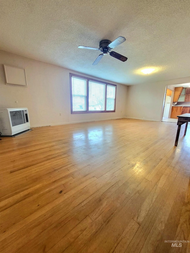 unfurnished living room with a textured ceiling, light wood-type flooring, heating unit, and ceiling fan