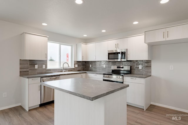 kitchen with appliances with stainless steel finishes, sink, white cabinetry, a kitchen island, and light hardwood / wood-style floors