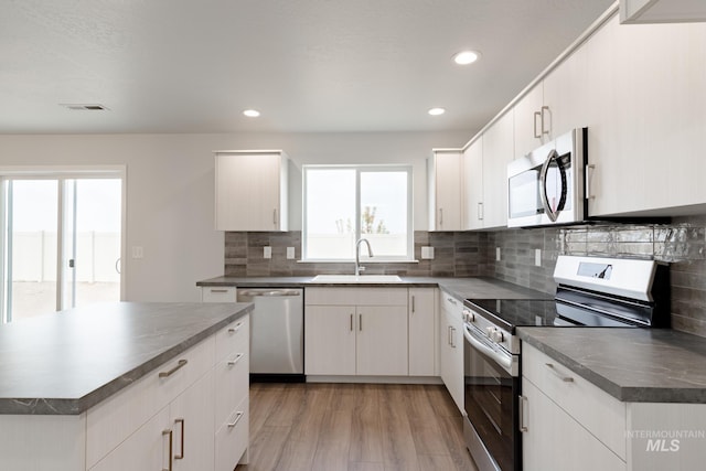 kitchen featuring light hardwood / wood-style flooring, appliances with stainless steel finishes, sink, white cabinetry, and decorative backsplash