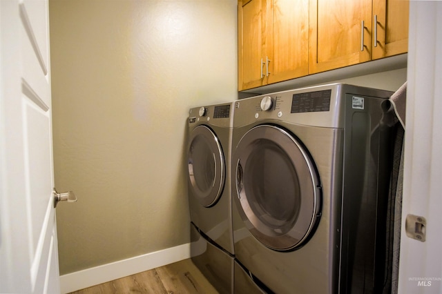 clothes washing area featuring light wood-type flooring, washer and dryer, and cabinets