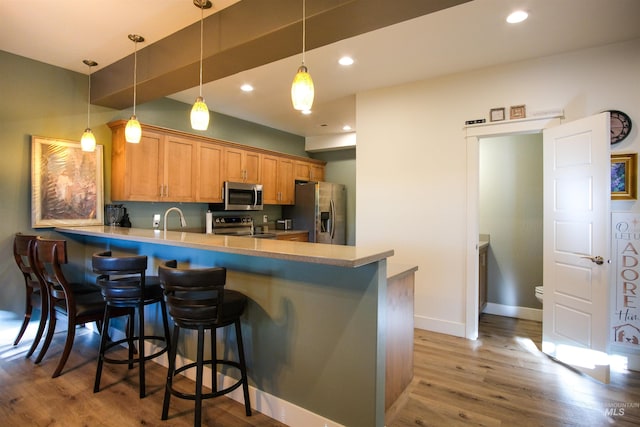 kitchen with a kitchen breakfast bar, kitchen peninsula, stainless steel appliances, wood-type flooring, and sink