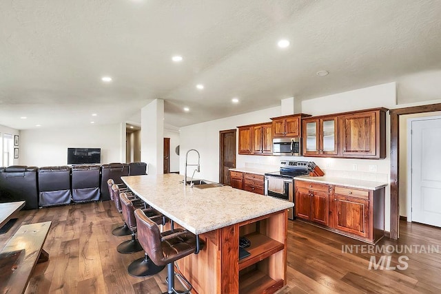 kitchen with brown cabinetry, dark wood-style flooring, a breakfast bar area, a sink, and stainless steel appliances