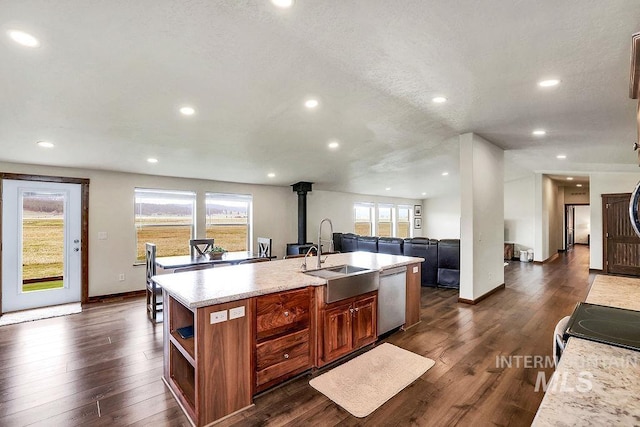 kitchen with a wood stove, a sink, stainless steel appliances, recessed lighting, and an island with sink