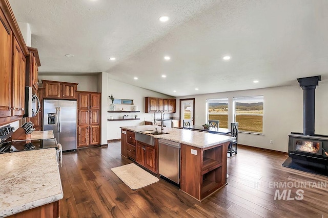 kitchen featuring brown cabinetry, open shelves, a kitchen island with sink, a sink, and stainless steel appliances