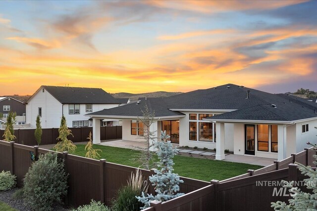 9989 W Bouvardia St, Star, ID 83669 - back of property at dusk featuring a patio area, a fenced backyard, stucco siding, and a shingled roof