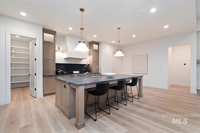 9989 W Bouvardia St, Star, ID 83669 - kitchen featuring dark countertops, a large island with sink, light wood-style floors, a kitchen bar, and recessed lighting