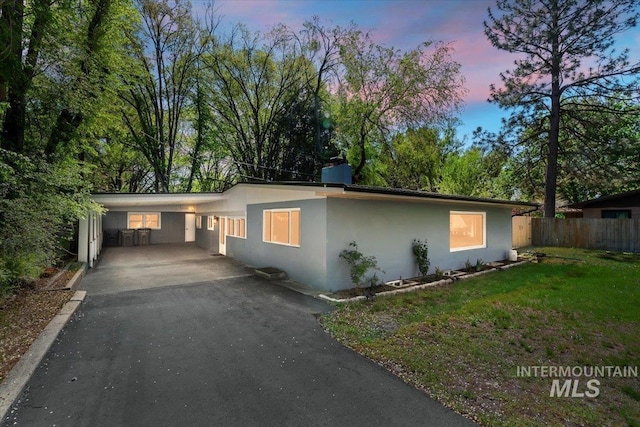 view of front of house featuring driveway, a front yard, stucco siding, fence, and an attached carport