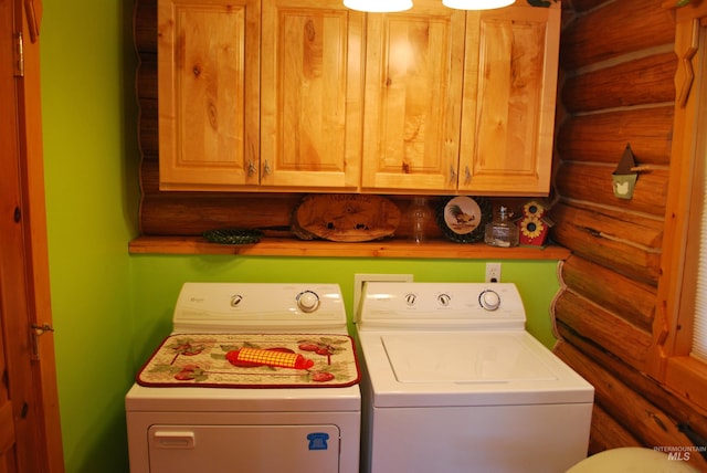 laundry area with log walls, washing machine and clothes dryer, and cabinet space