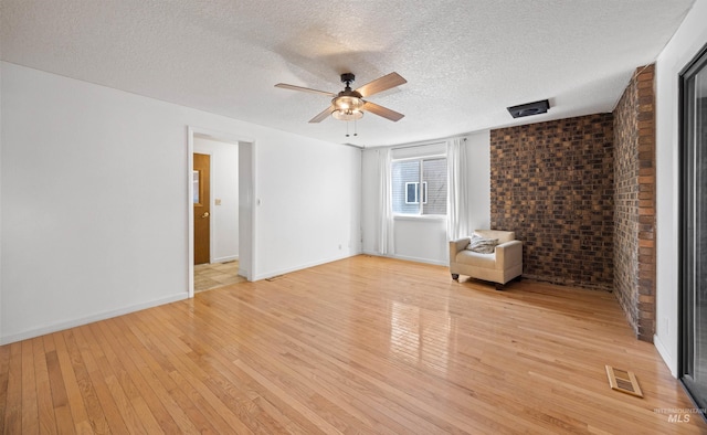 unfurnished room featuring a ceiling fan, a textured ceiling, brick wall, visible vents, and light wood-type flooring